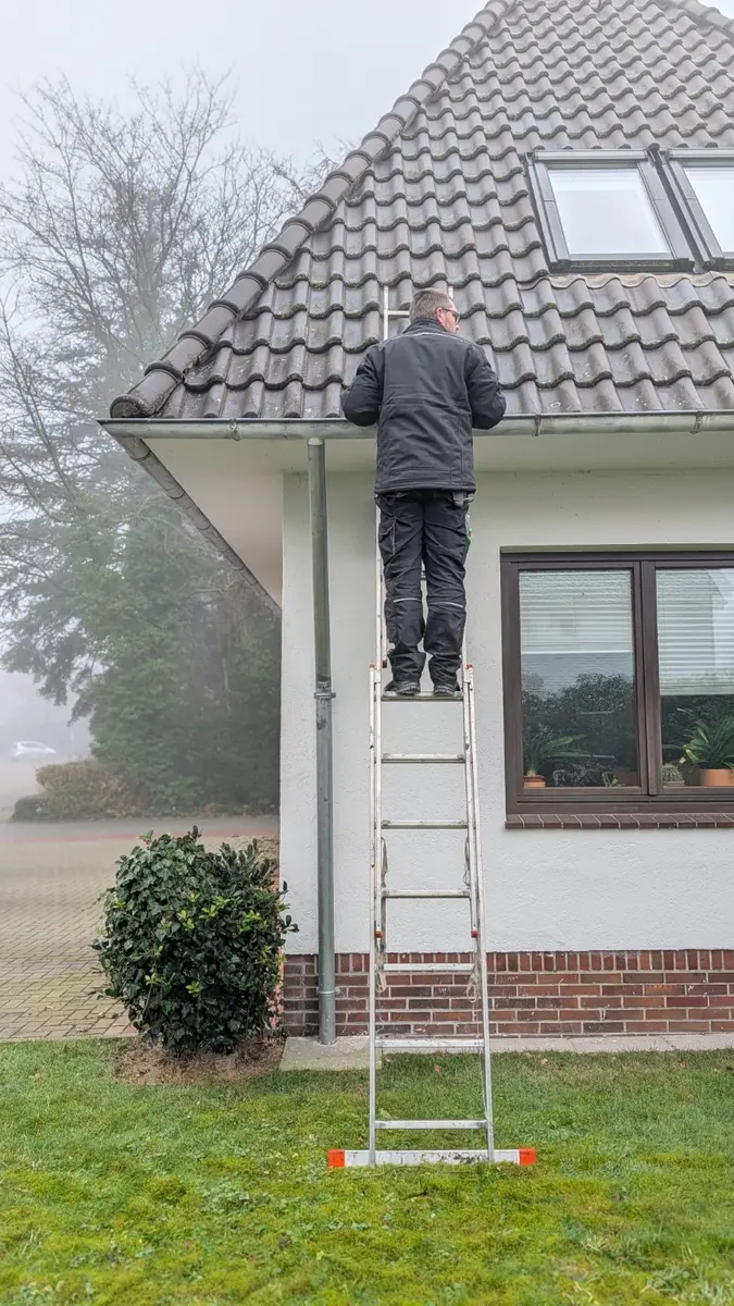 Kontrolle und Pflege einer Dachrinne an einem Wohnhaus